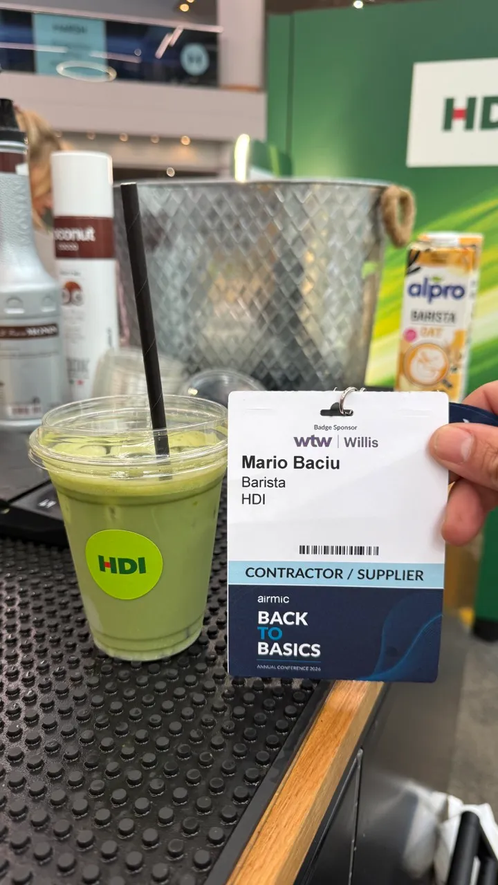 Green iced drink in a clear cup with a black straw beside a name badge reading 'Mario Baciu, Barista, HDI'